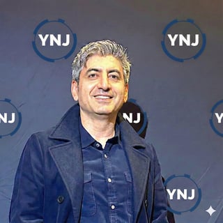 Middle-aged man with gray hair wearing a dark blue jacket at a YNJ branded media event backdrop